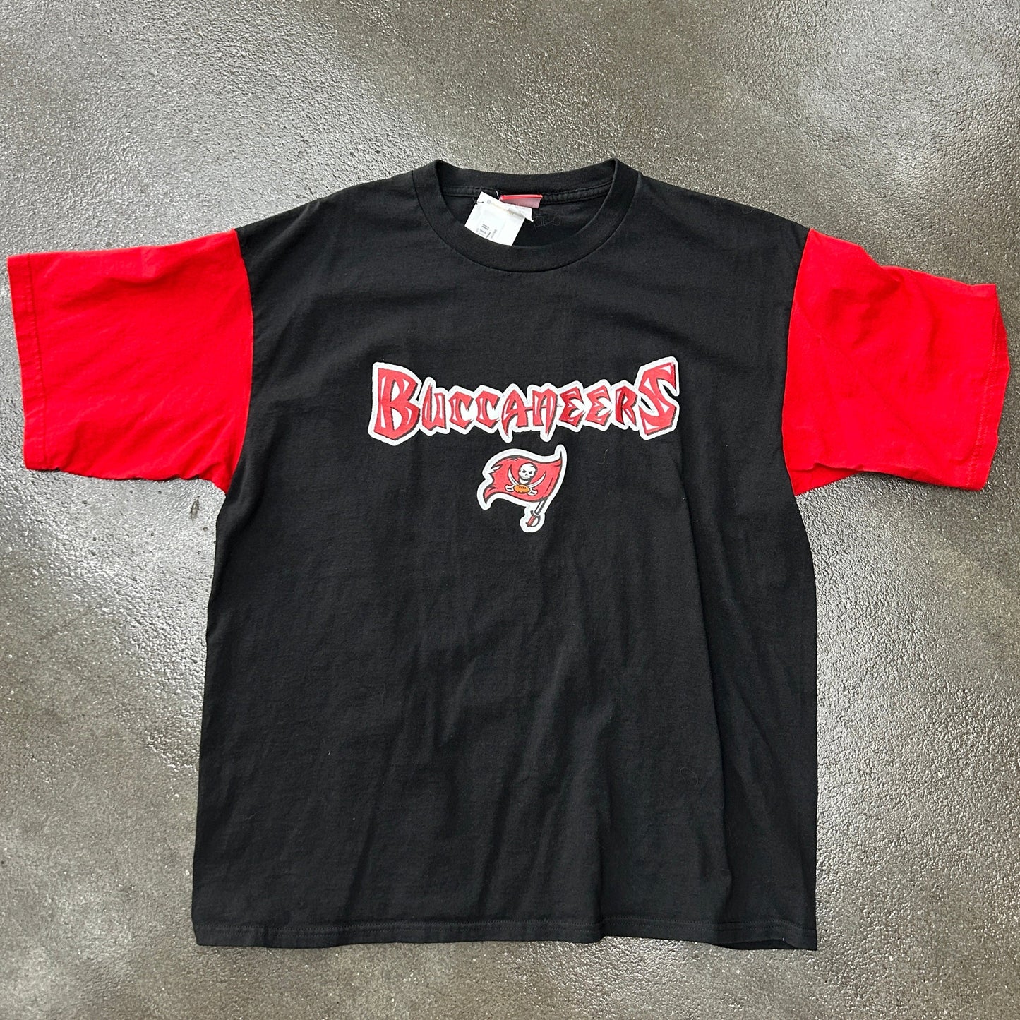 Black t-shirt with red sleeves and 'Buccaneers' logo on a gray surface
