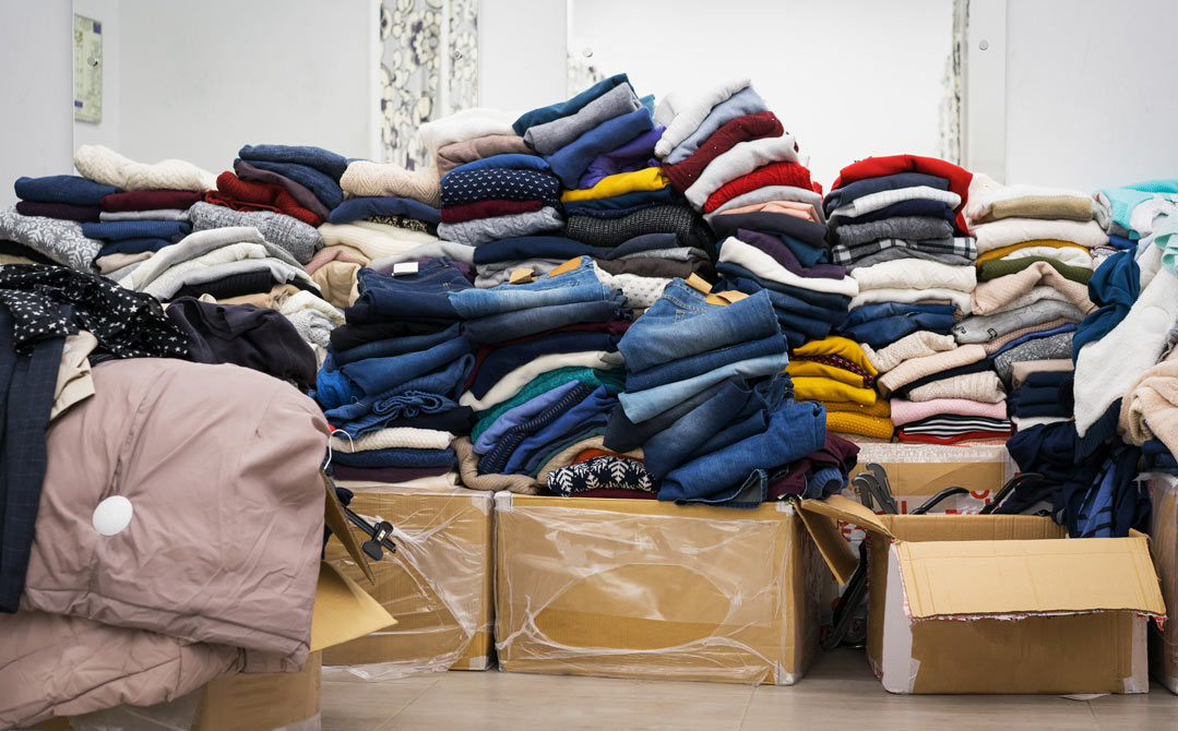 Piles of used clothing; jeans, sweaters, tops, crewnecks etc in boxes