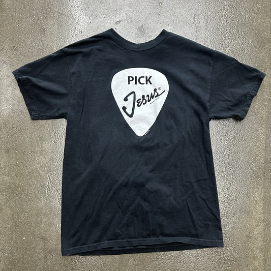 Black t-shirt with a white guitar pick graphic and 'Pick Jesus' text on a gray surface